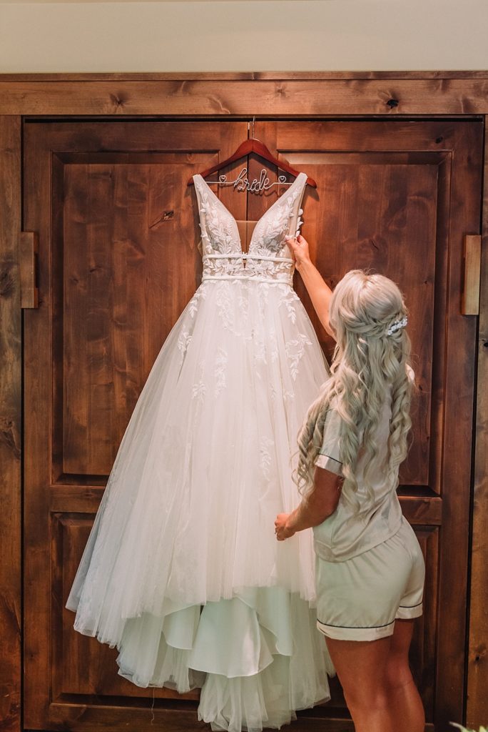 Bride admires her wedding dress as it hangs on the closet doors