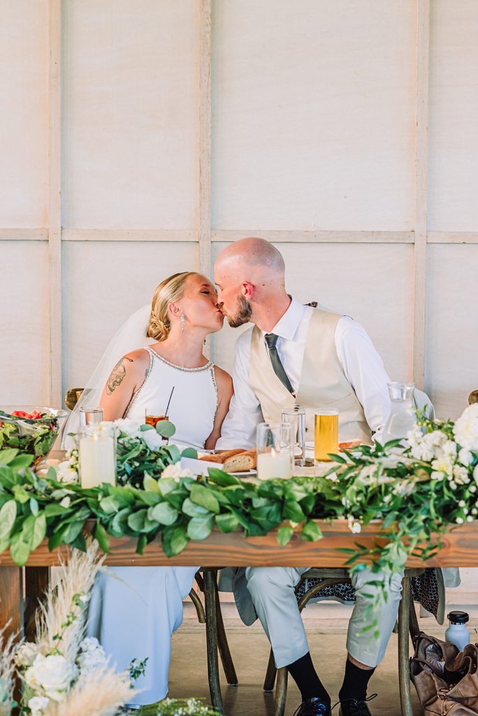 couple kisses at head table during wedding dinner