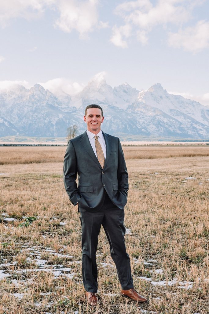 groom in golden fields with mountain behind