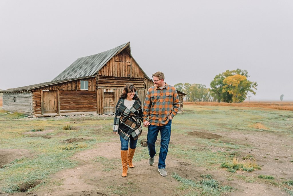 couple walk and hold hands in front of Mormon Row Barn