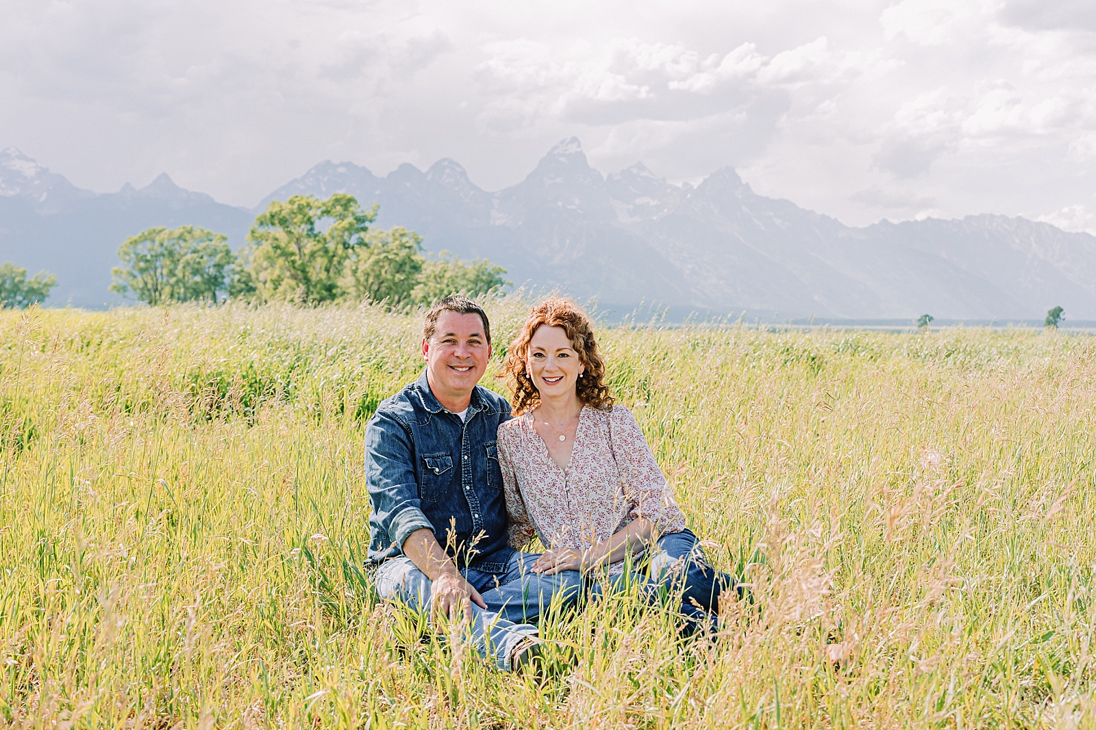 Couple sitting in field in front of the Teton mountains