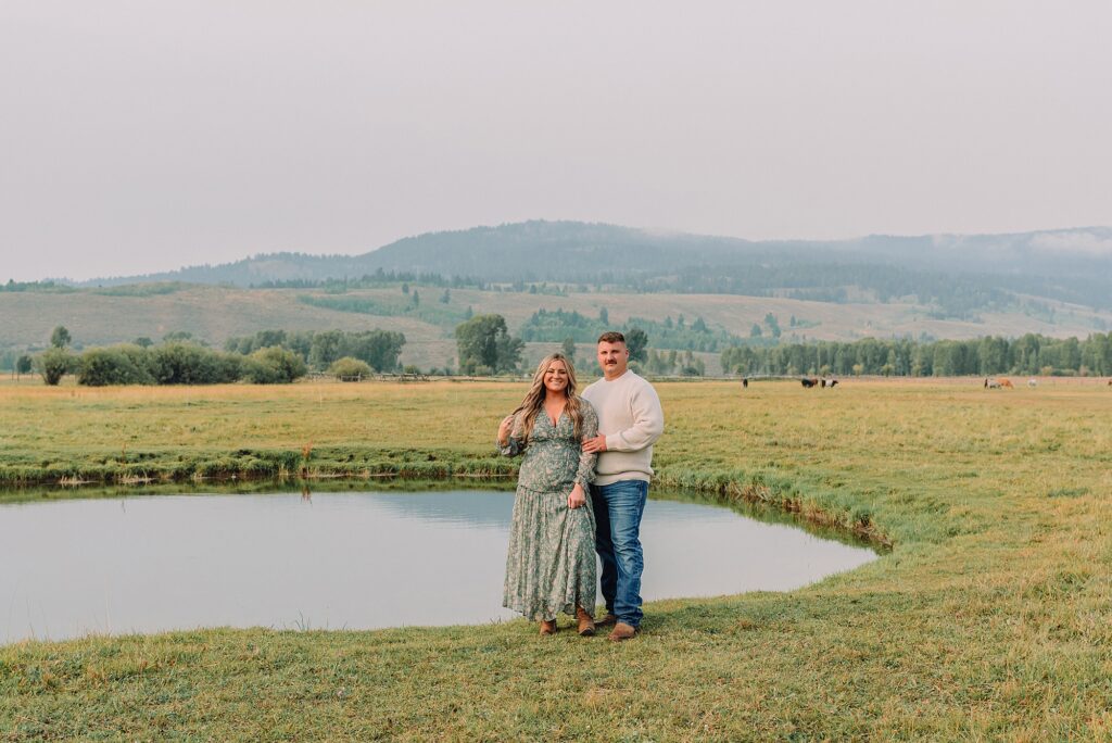 Engaged Couple pose in front of pond in field at Diamond Cross Ranch