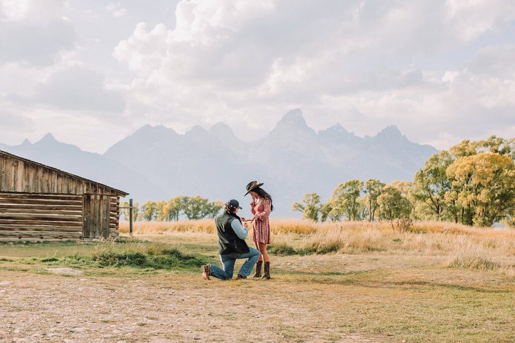 man proposes to girlfriend in fall mormon row proposal with golden grasses and the Teton Mountains