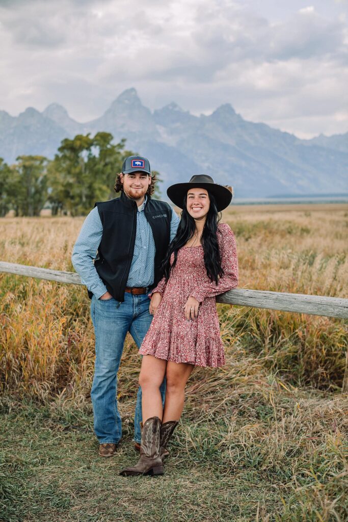 newly engaged couple pose in golden field with the Teton mountain range in the background