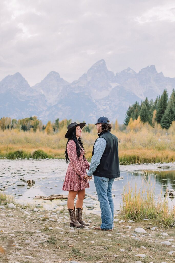 man and woman pose with hats at schwabacher landing during engagement photos