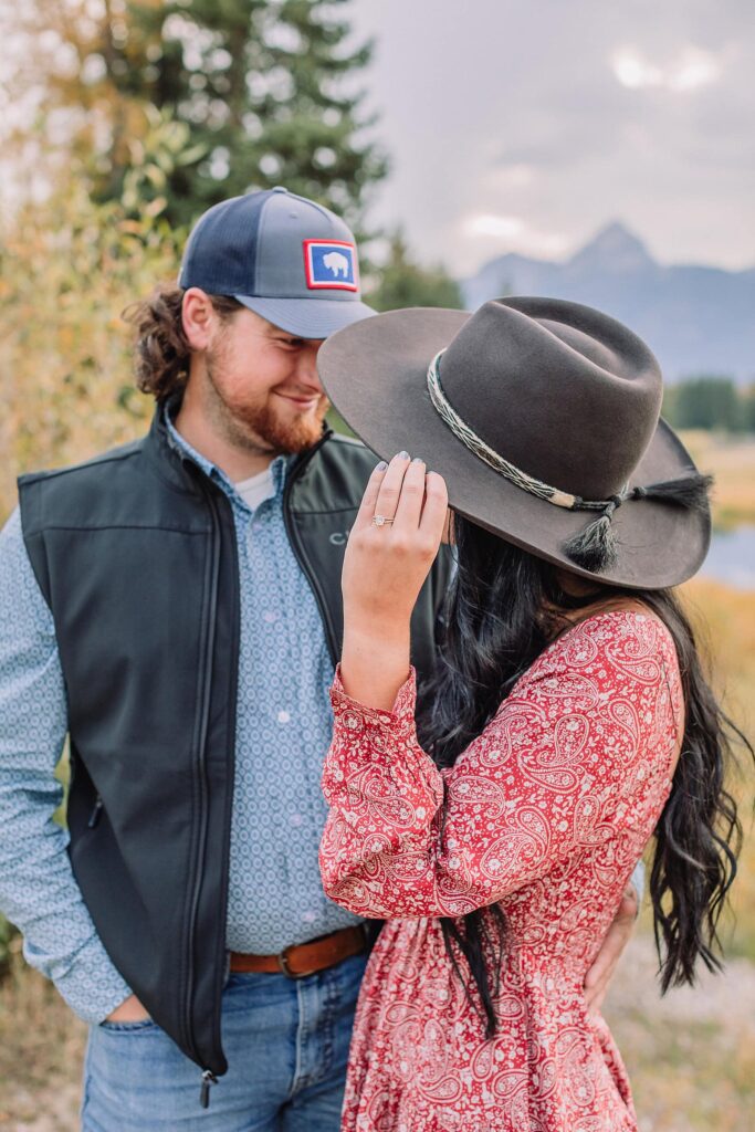 man and woman pose with hats at schwabacher landing during engagement photos