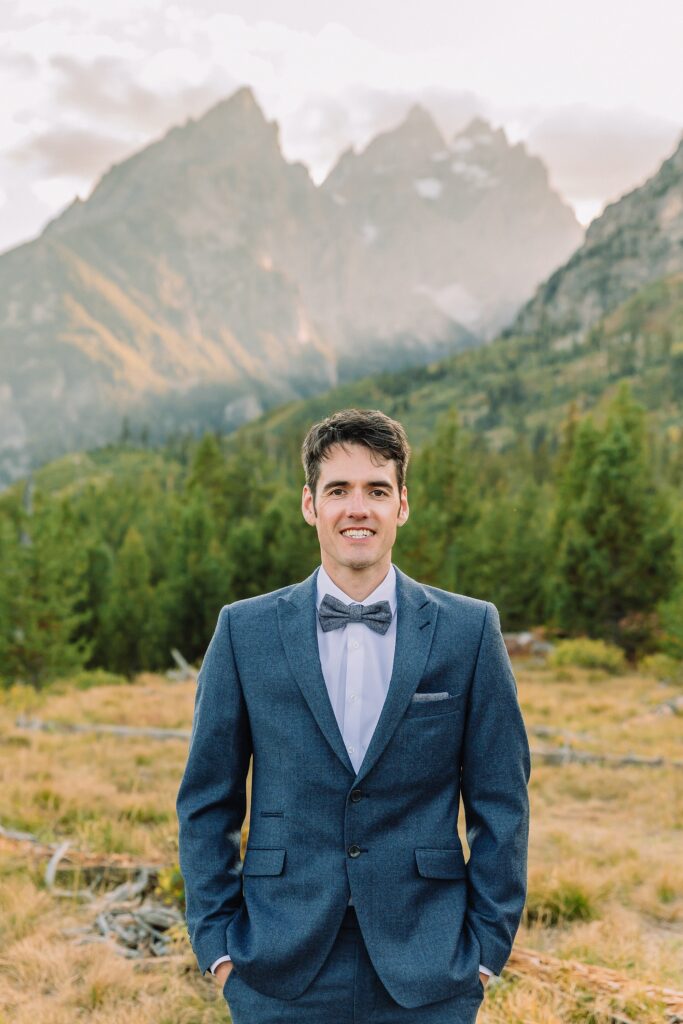 groom poses in blue wedding suit at String Lake in Jackson Hole