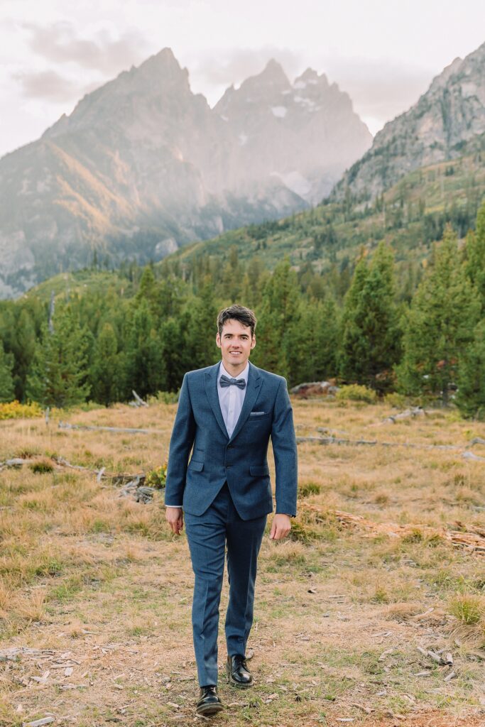 groom poses in blue wedding suit at String Lake in Jackson Hole
