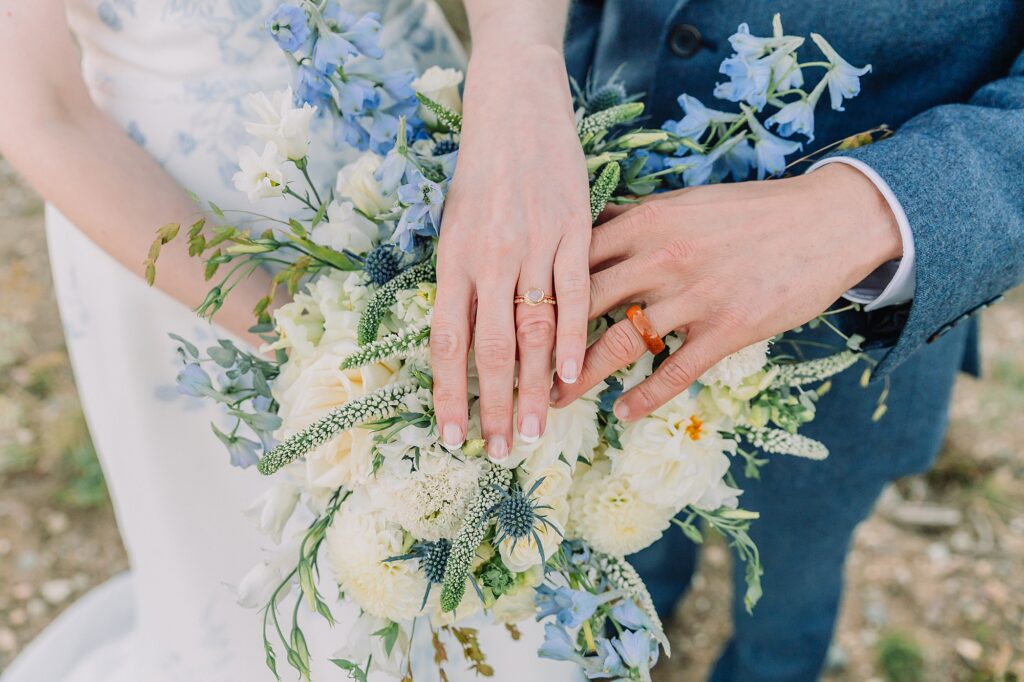 hands showcasing wedding rings with blue and cream bouquet.