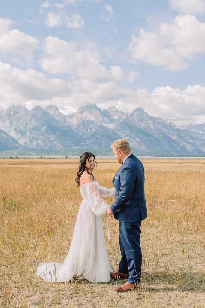 bride and groom share pre-ceremony first look in a field with the Teton mountains behind them
