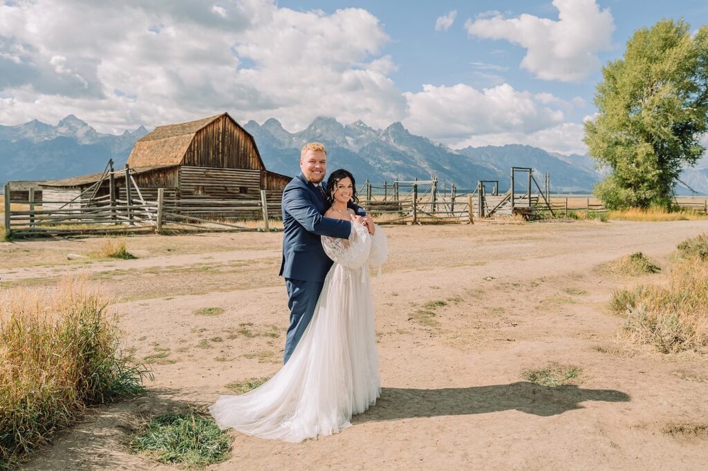 wedding couple stands in front of the mormon row barn, John Moulton barn and the Tetons