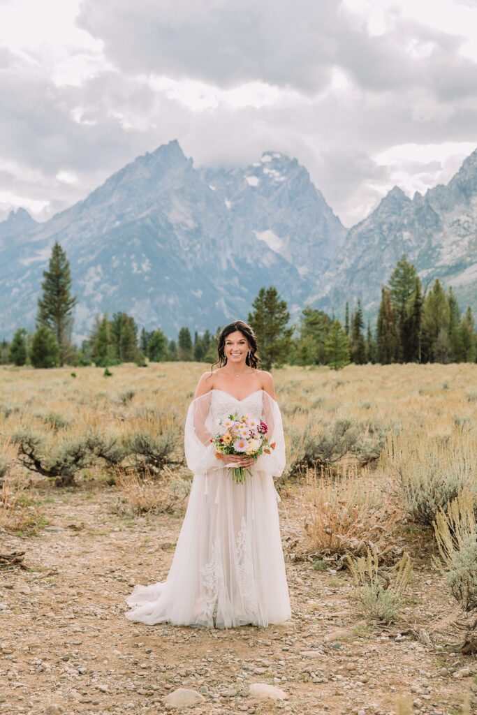bride poses in front of mountain scene in wedding dress and bouquet