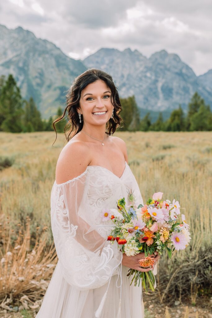 bride poses in front of mountain scene in wedding dress and bouquet
