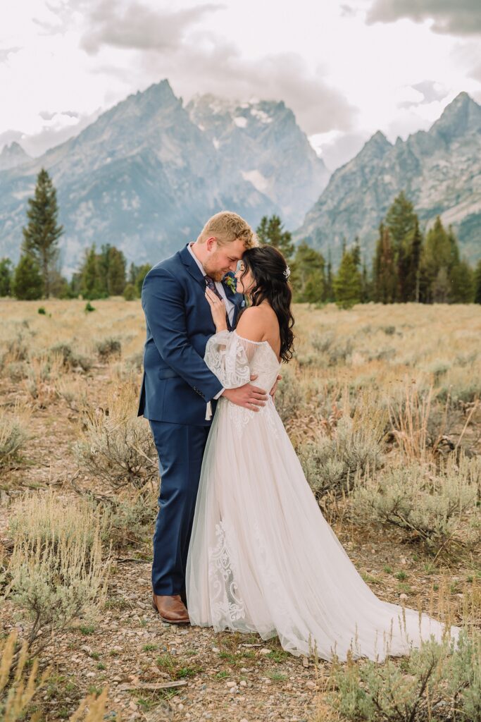 bride and groom snuggle romantically at mountain view turnout in wedding attire