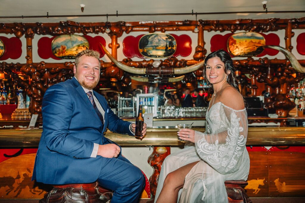 bride and groom share pre-dinner drinks at the million dollar cowboy bar while sitting on saddle chairs