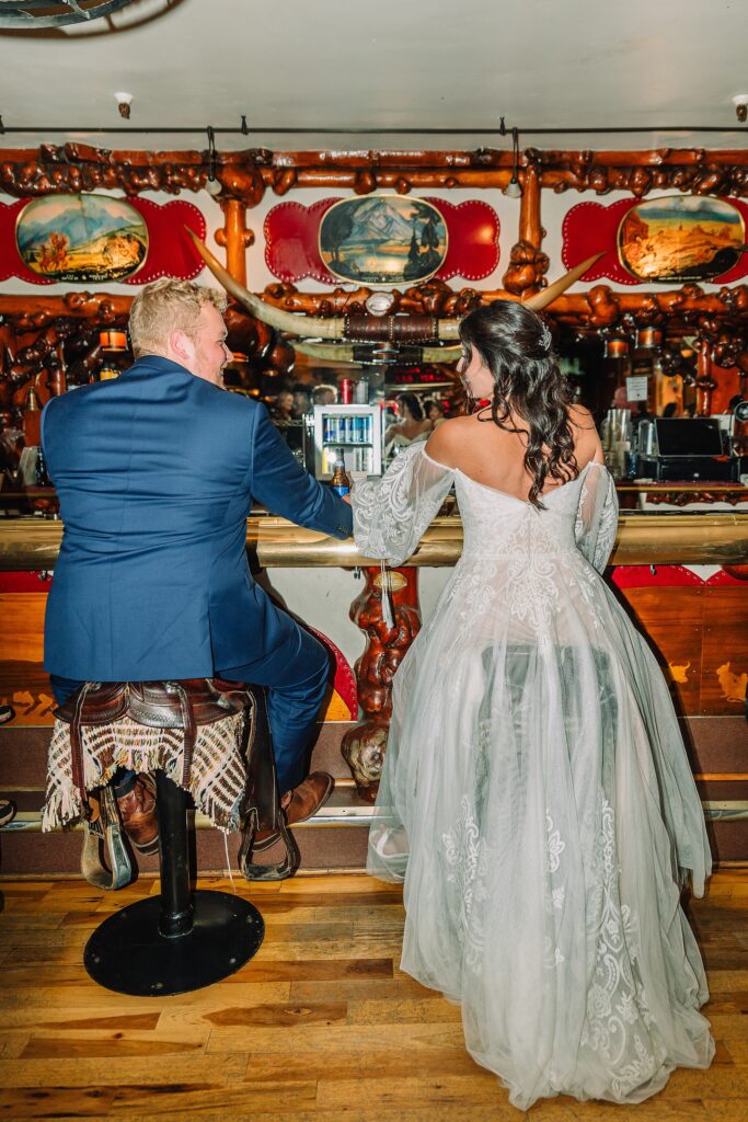 bride and groom share pre-dinner drinks at the million dollar cowboy bar while sitting on saddle chairs