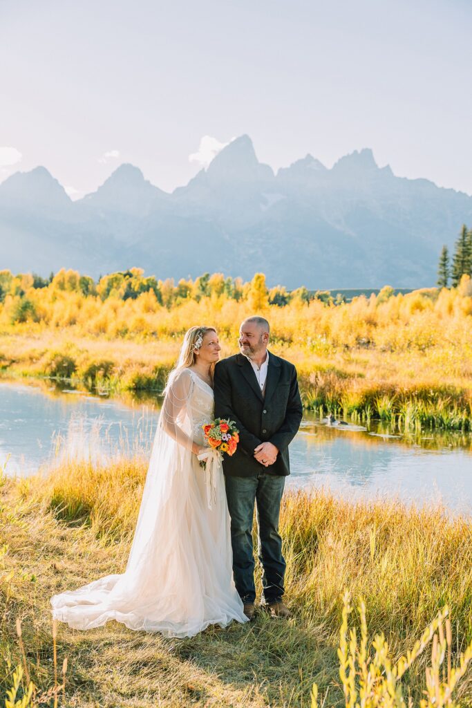 Jackson Hole honeymoon wedding photos Schwabacher Landing wedding portraits Snake River wedding photography September mountain wedding photos beaded wedding dress golden hour western groom style wedding photos Teton mountain wedding portraits sheer cape wedding dress photography
