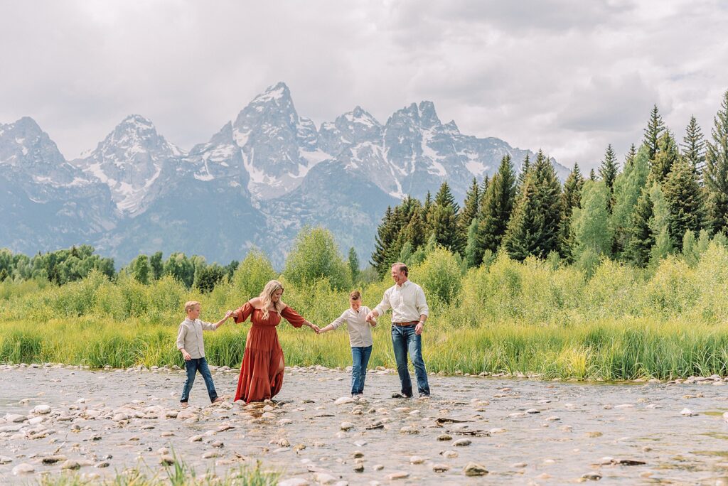 family playing in water during professional photo session Grand Teton sunrise family portraits at Schwabacher Landing cream and rust color palette mountain family photos Grand Teton vacation photographer coordinating family outfits without matching