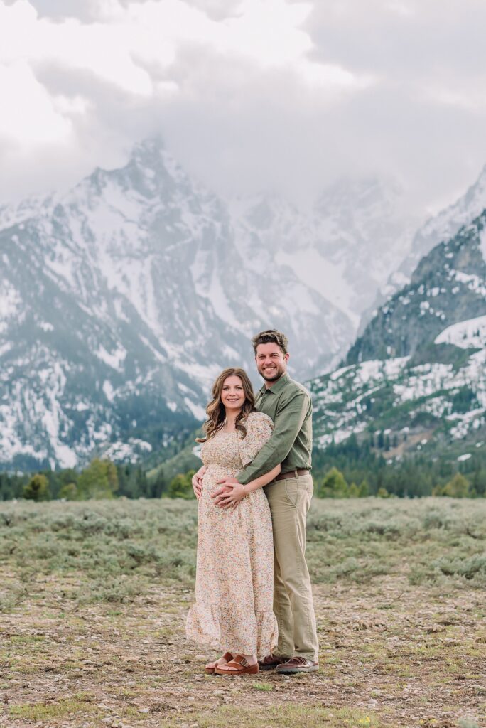 Jackson Hole babymoon maternity photos at Cathedral View Turnout Grand Teton National Park maternity session in spring Cathedral View Turnout couple photos snow capped peaks Flowery maternity dress mountain photography Jackson Hole Jackson Hole Maternity Photographer