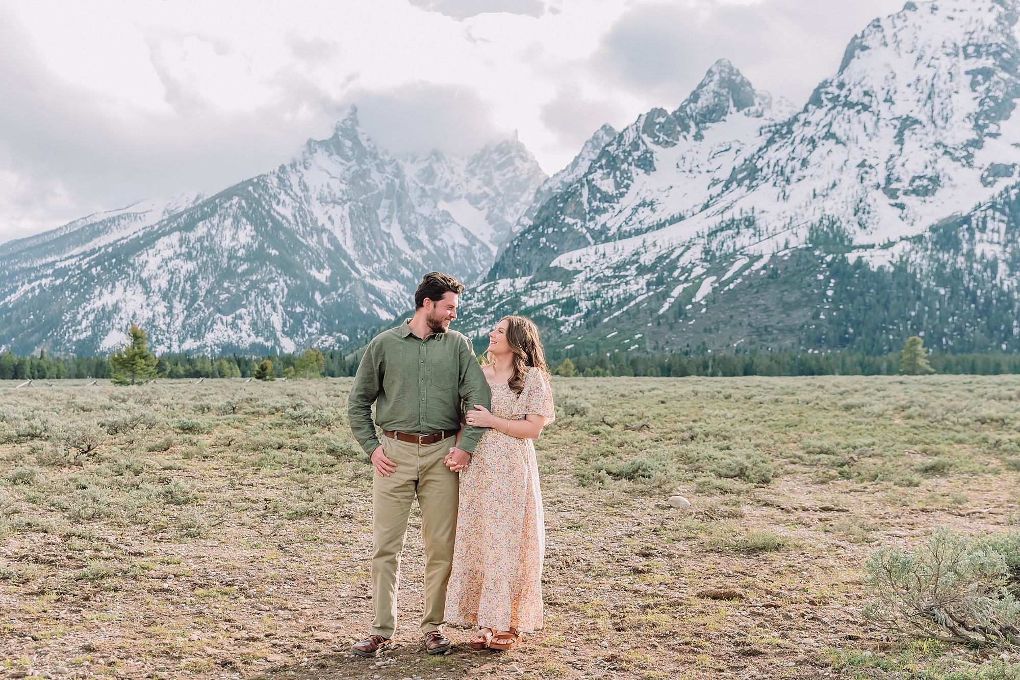 Jackson Hole babymoon maternity photos at Cathedral View Turnout Grand Teton National Park maternity session in spring Cathedral View Turnout couple photos snow capped peaks Flowery maternity dress mountain photography Jackson Hole Jackson Hole Maternity Photographer