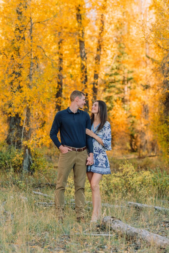 Jackson Hole engagement photos at Schwabacher Landing fall colors couple portraits along Snake River Wyoming autumn surprise engagement session Grand Teton National Park western hats engagement photos Jackson Wyoming fall engagement photos sagebrush Tetons backdrop blue dress engagement photos Jackson Hole Wyoming Schwabacher Landing couples photography fall season golden cottonwood trees engagement portraits Wyoming