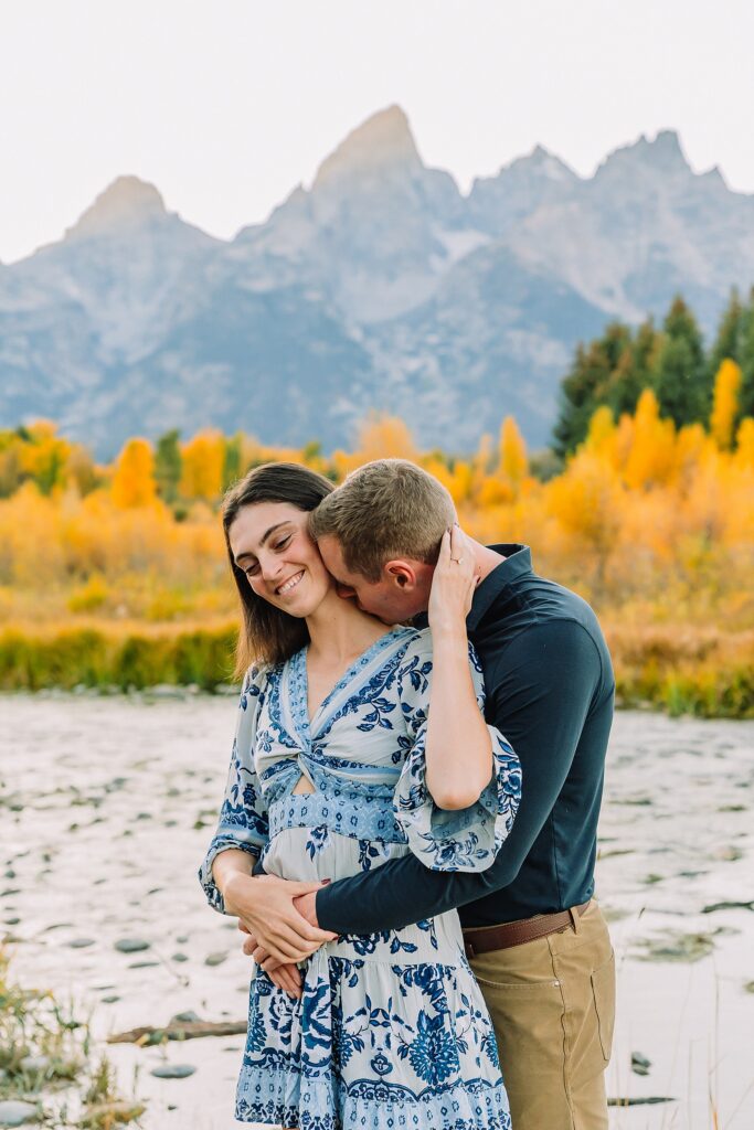 Jackson Hole engagement photos at Schwabacher Landing fall colors couple portraits along Snake River Wyoming autumn surprise engagement session Grand Teton National Park western hats engagement photos Jackson Wyoming fall engagement photos sagebrush Tetons backdrop blue dress engagement photos Jackson Hole Wyoming Schwabacher Landing couples photography fall season golden cottonwood trees engagement portraits Wyoming